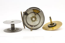 Load image into Gallery viewer, Antique brass faced fishing reel with a center decorative disc and a yellow handle, showing signs of aging and use. 1906 brass faced perfect against a white background. this shows the inside of the reel and you can see the ball bearings