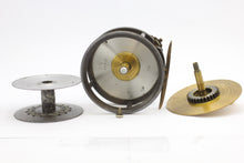Load image into Gallery viewer, Antique brass faced fishing reel with a center decorative disc and a yellow handle, showing signs of aging and use. 1906 brass faced perfect against a white background, this image shows the inside of the reel